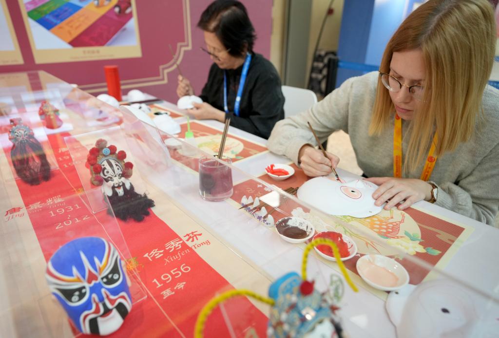 10月16日，在第三屆“一帶一路”國際合作高峰論壇新聞中心，來自比利時(shí)的記者（右）體驗(yàn)畫京劇臉譜。新華社記者 王毓國 攝