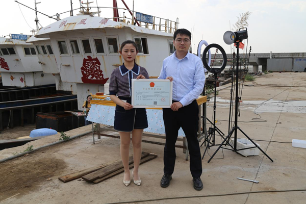 海鮮電商張夢琴與幫辦員手持食品經(jīng)營許可證合影。贛榆區(qū)委宣傳部供圖